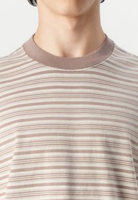 T-shirt rayé en tissu doux avec des rayures alternées fines marron et beige, doté d'un col rond côtelé assorti.
