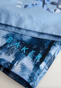 Tela azul con estampado de palmeras. Presenta un texto audaz "BAKER" en turquesa. Textura suave con borde doblado, diseño limpio y colores vibrantes.