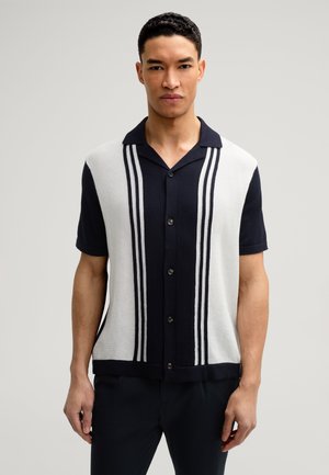 Chemise en tricot à col marin et blanc à manches courtes, avec des rayures verticales et des boutons sur le devant, motif texturé sur le tissu.