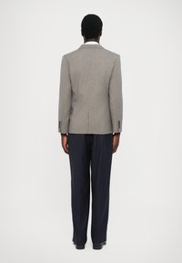 Szürke kockás zakó, két gombbal, tengerészkék csíkos nadrággal és fekete cipővel párosítva. Hátsó nézetből látható.