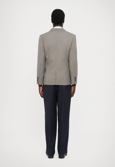 Grau karierter Sakkok mit zwei Knöpfen, kombiniert mit navy gestreiften Hosen und schwarzen Schuhen. Von hinten betrachtet.