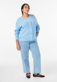 Svetlomodrý rebrovaný kardigán so zlatými gombíkmi, v kombinácii so svetlomodrými pruhovanými džínsami a tmavohnedými balerínkami. Hladká textúra, voľný strih.