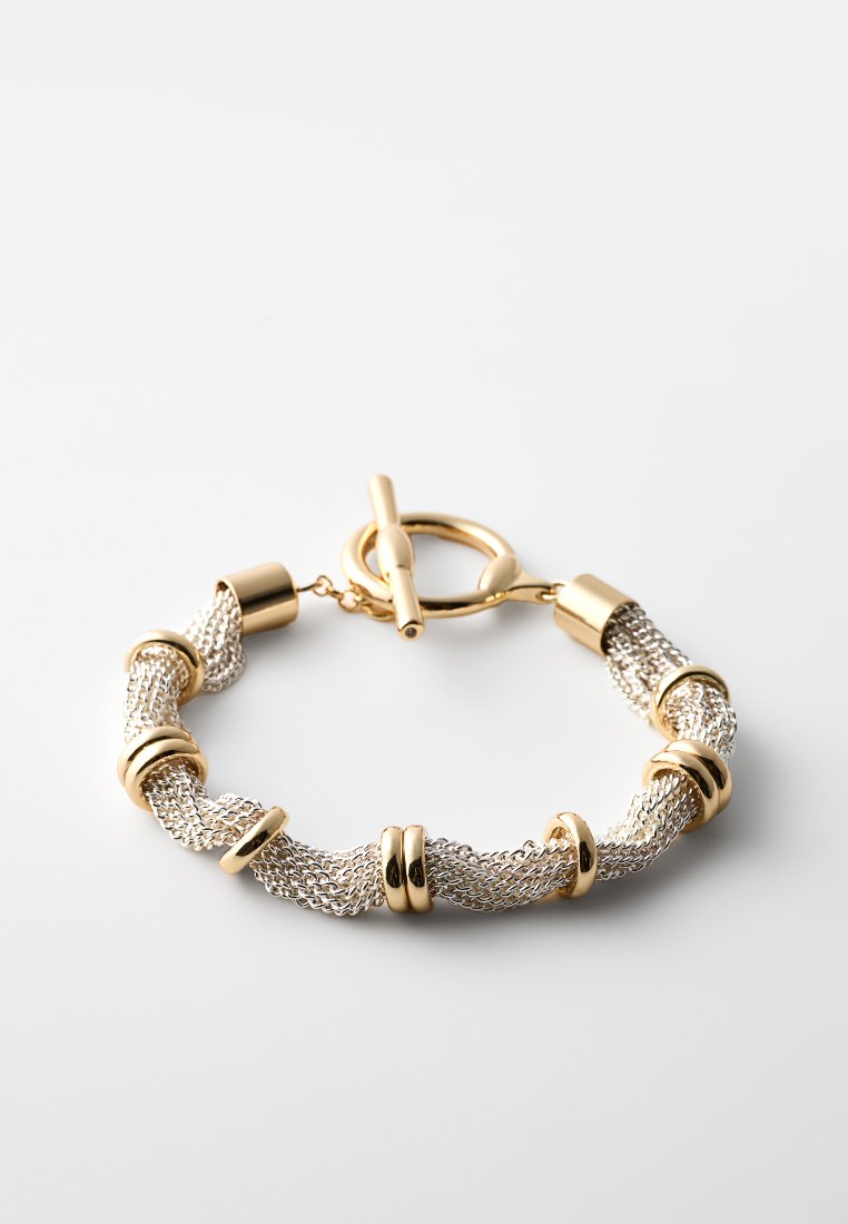 Bracelet en maille torsadée en or et argent avec plusieurs anneaux en or et un fermoir à bascule sur un fond blanc uni.