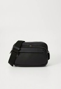 Černá kabelka přes rameno z texturované kůže s přední kapsou na zip, nastavitelným popruhem a jemným zdobením značky na přední straně.