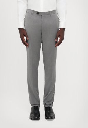 Pantalons de costume gris en tissu texturé, avec une coupe slim et une fermeture à un bouton. Associés à des chaussures noires en cuir.