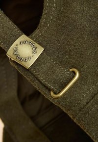 Brūns vilnas filca siksniņa ar zelta toni apzeltītu Joules logotipa metāla detaļu un šuvju akcentiem. Aprīkota ar metāla loku, lai regulētu izmēru.