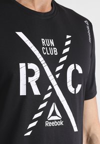 Mustapaita, jossa on pyöreä kaula-aukko, sisältää valkoiset "RUN CLUB" -tekstit ja viistot raidoitukset. Hihassa on Reebok-logo.