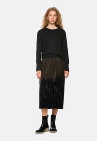 Schwarzes Langarmshirt kombiniert mit einem plissierten Rock mit gepunktetem Muster, dunkler Farbpalette und Stiefeletten mit dicker Sohle.
