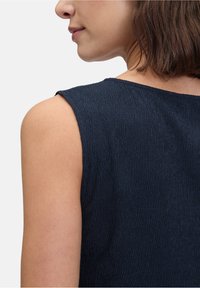 Marineblauwe mouwloze top van een textuurstof met een gladde, ronde halslijn. De stof vertoont verticale ribbeldetails.