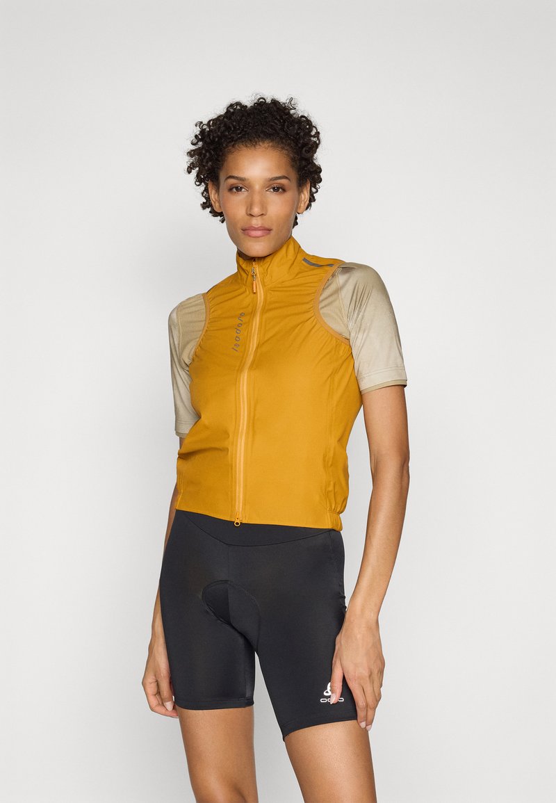Kurzärmlige Radjacke in senfgelb, aus leichtem Stoff mit hohem Kragen und Reißverschluss. Kombiniert mit schwarzen gepolsterten Radshorts.