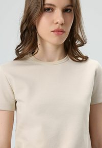 Beige cotton t-shirt with a crew neck, short sleeves, smooth texture, and a fitted shape, showing minimal seams and no visible branding.