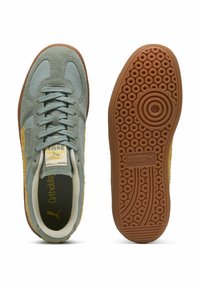 Baskets Puma avec une tige en daim bleu clair, des accents latéraux jaunes et une semelle en caoutchouc caramel présentant un motif circulaire et un détail de marque.