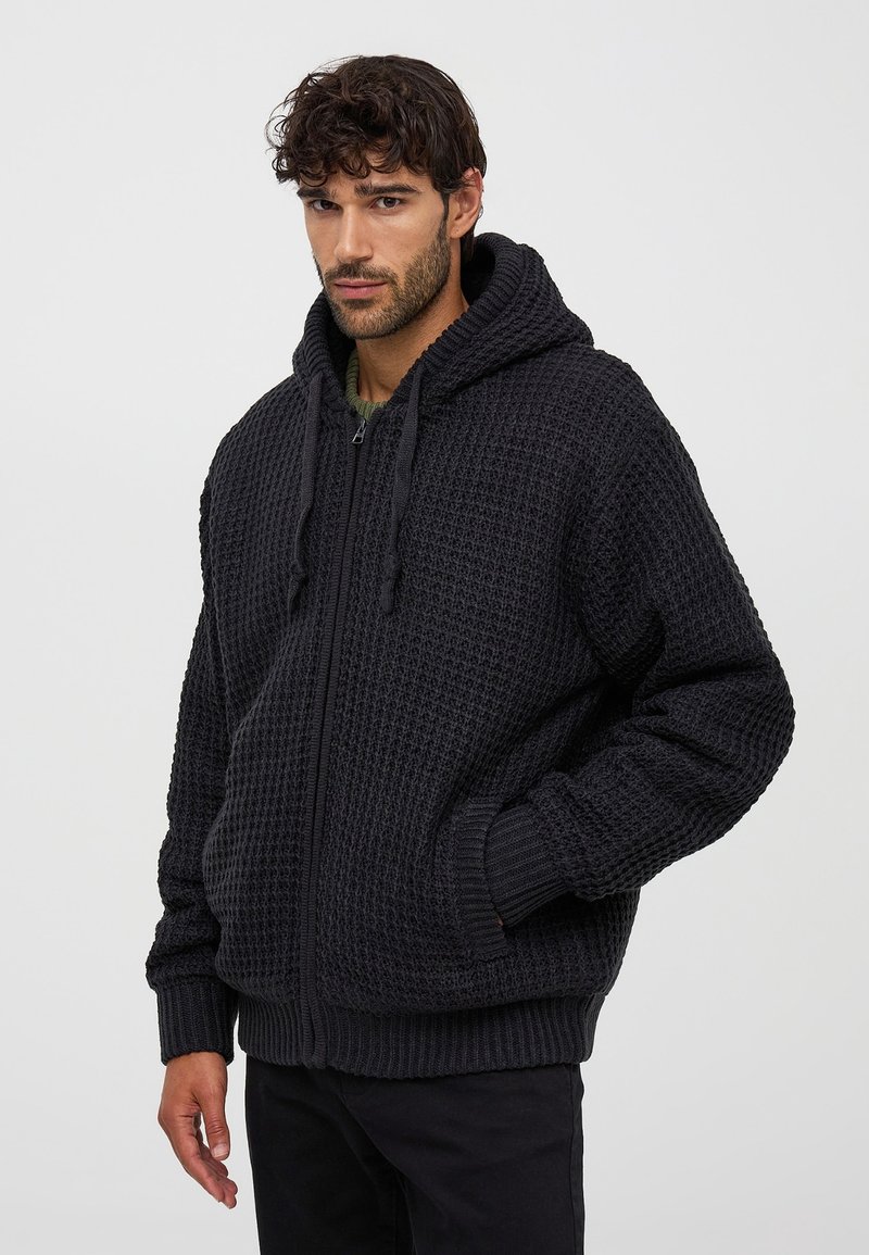 Czarna, zakładana na zamek kurtka z kapturem, z teksturowanym wzorem dzianiny, prążkowanymi mankietami i dołem, z troczkami i bocznymi kieszeniami.