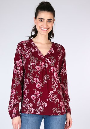 Burgundy floral blouse with long sleeves, V-neck, and gathered cuffs. Features pink flowers and green leaves on a textured fabric.