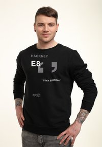Felpa nera con scollatura a girocollo con testo grafico: "HACKNEY", "E8" e "STAY SURREAL." Logo del marchio ben visibile sulla parte anteriore in basso.