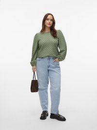 Rohelise tekstuuriga pika varrukaga pluus, millel on õlgadel patšid, helesinised kõrge vöökohaga teksad, mustad loafersid ja väike pruun käekott.