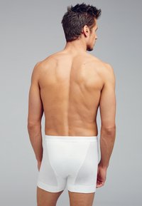 Boxer shorts bianchi in cotone indossati da un uomo, con un design semplice, forma aderente e texture morbida. Lo sfondo è grigio.