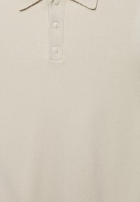 Polo beige avec un col et trois boutons sur la patte, montrant un tissu texturé en gros plan.