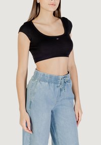 Top corto nero con scollo a U e maniche corte. Abbinato a pantaloni in denim azzurro chiaro, larghi, con vita elasticizzata.