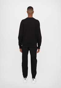 Felpa nera e pantaloni jogger coordinati, entrambi con una vestibilità rilassata. Presentano polsini e vita elasticizzati. Sneakers bianche con dettagli neri.