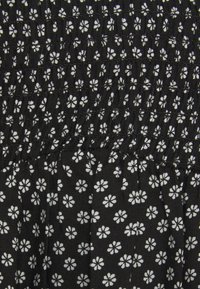 Schwarzer Stoff mit einem weißen Blumenmuster, der eine geraffte Textur und Rüschendetails aufweist. Kleinere weiße Blütenmuster bedecken die Oberfläche.