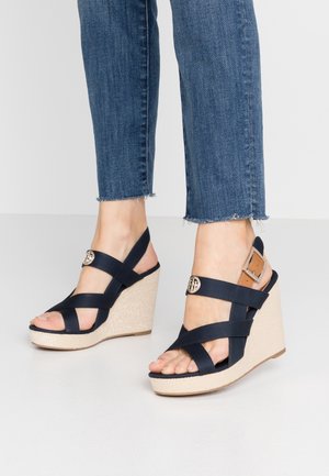 Marineblå kilehælssandaler med krydsremdesign, der har en struktureret beige platform og en guldfarvet detalje på remmen.