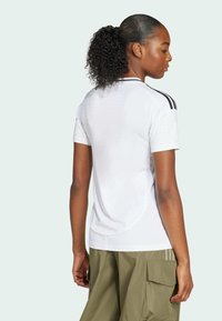 White athletic t-shirt with black stripes on shoulders, round neckline, and breathable mesh texture. Paired with olive green cargo pants.
