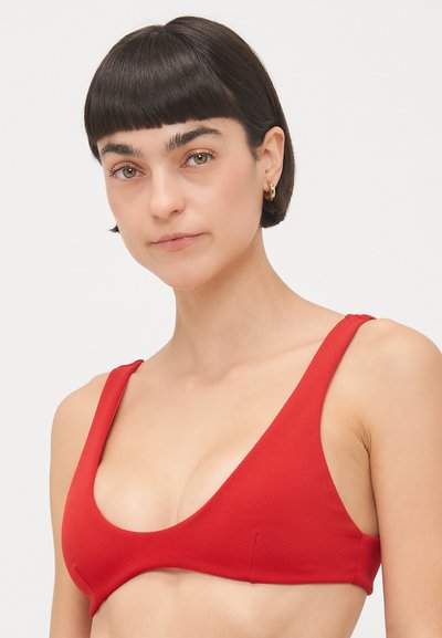 Haut de bikini rouge en tissu doux avec un design décolleté, des larges bretelles et des coutures minimales. Caractéristiques d'une texture lisse et d'une forme triangulaire.