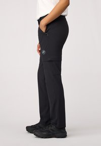 Pantalons de randonnée noirs en tissu extensible, dotés de poches zippées et d'une étiquette logo. Coupe droite avec des coutures pour un look ajusté.