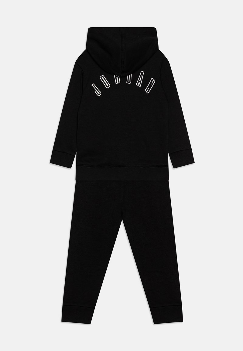 Set di felpa nera con cappuccio e pantaloni abbinati, caratterizzato da polsini a coste e logo "JORDAN" in bianco sulla schiena. Materiale morbido con un design minimale.