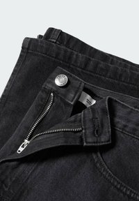 Jean en denim noir avec une fermeture éclair argentée, une fermeture à bouton et une surface lisse légèrement texturée. Ouverture de poche avant visible.