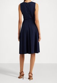 Granatowa sukienka bez rękawów z dopasowanym górnym elementem i rozkloszowanym dołem, z tylnym zamkiem błyskawicznym i gładką, teksturowaną tkaniną.
