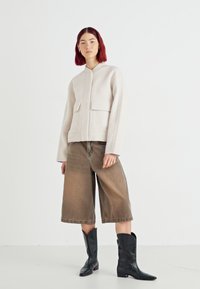 Lysbeige cropped jakke med to frontlommer, parret med løse brune denim culotter og sorte western-inspirerede ankelstøvler.
