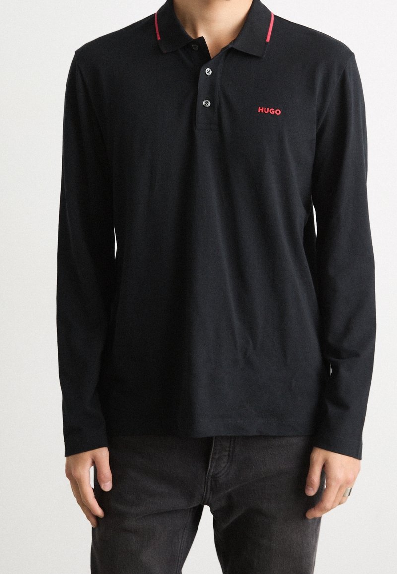 Schwarzes Langarm-Poloshirt mit rotem Kragenstreifen und rotem "HUGO"-Logo. Hergestellt aus weichem Stoff mit klassischer Passform, ideal für die Freizeit.