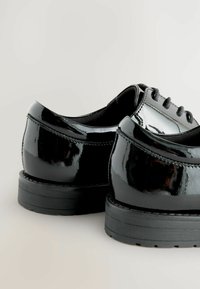 Chaussures en cuir verni noir avec une finition brillante, design à lacets, bout arrondi et semelle en caoutchouc plate présentant un motif de traitement texturé.