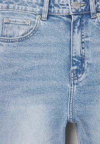 Jean en denim bleu clair avec une taille haute, un design à cinq poches, une fermeture à bouton métallique et des détails de surpiqûres visibles avec une texture légèrement délavée.