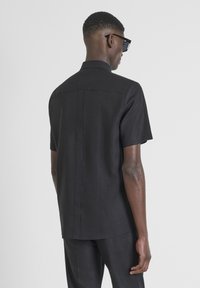 Camisa negra de manga corta en una mezcla de lino. Presenta un corte recto, cuello y detalles de costura en la parte trasera. Diseño simple y minimalista.