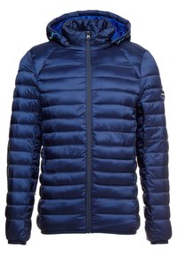 Marineblauwe pufferjas met capuchon, ritssluiting en geribbelde manchetten. Gemaakt van glad, doorgestikt stof met een glanzende afwerking en een blauw binnenvoering.