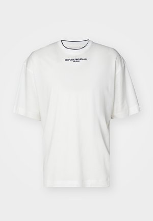 Valkoinen ylisuurikokoinen lyhythihainen T-paita, jossa on musta "EMPORIO ARMANI MILANO" -logo pyöreän, mustareunaisen pääntien alapuolella keskitettynä.
