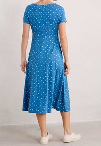 Blå klänning med prickar, korta ärmar, figursydd överdel, utsvängt nederdel och mjuk textur. Stiliserad med avslappnade vita sneakers.