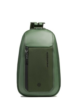Mochila compacta de hombro verde con bolsillo delantero con cremallera y correa ajustable, con panel texturizado y marca sutil.