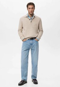 Beżowy sweter dziany z kołnierzem, połączony z jasnoniebieskimi dżinsami. Czarne mokasyny dopełniają strój. Prosty, codzienny design.