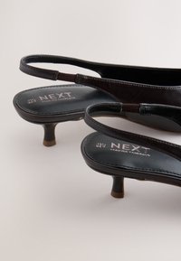 Paar schwarze Leder Slingback-Kitten-Heel-Schuhe mit ""NEXT"" Branding auf den Innensohlen vor neutralem Hintergrund.