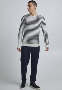 Pull rayé bleu marine et crème avec un col rond, des manches longues et des poignets côtelés. Associé à un pantalon bleu marine et des baskets noires.