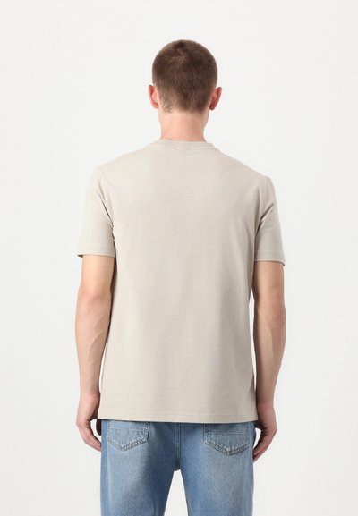 T-shirt beige clair à manches courtes en coton doux. Il présente un col rond et une coupe droite, porté avec un jean en denim bleu.