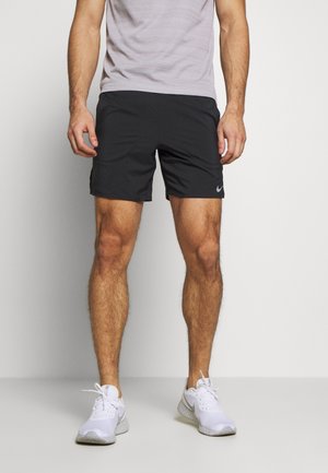 Schwarze Nike-Shorts aus einem glatten, leichten Stoff; mit Seitentaschen und einem kleinen Logo am linken Bein. Kombiniert mit weißen Sportschuhen.