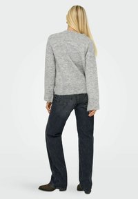 Pull gris surdimensionné avec une finition texturée, col rond et manches longues, associé à un jean à jambes larges bleu foncé et des bottes marron.