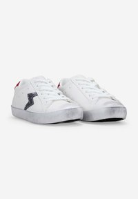 White sneakers with a textured gray sole, featuring a sparkly black lightning bolt design and red accents on the heel.