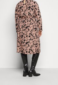 Pitkähihaiset mekko musta- ja vaaleanpunakukkaiskuvio, korkea vyötärö, avauma selässä ja yhdistetty polvimittaisiin mustiin saappaisiin.