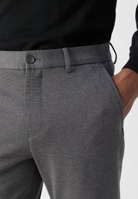 Sive hlače z gladko teksturo, ki imajo klasičen dizajn, poševne sprednje žepe in zapenjanje z gumbom na pasu.